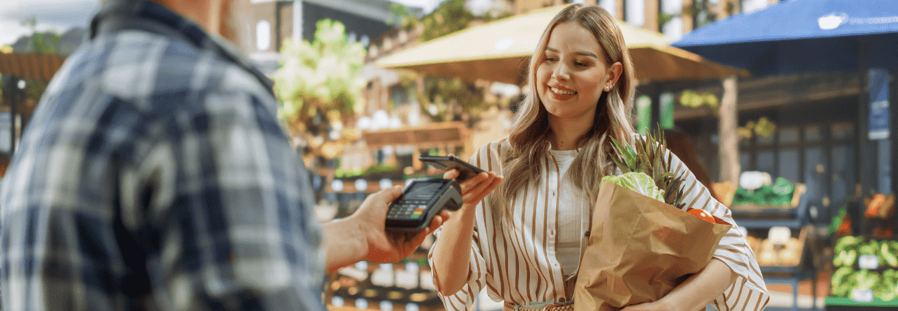 A woman shopping at a market making a contactless payment.
